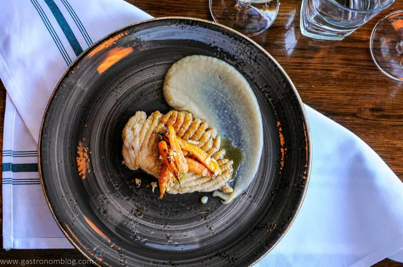 Top shot of gray pottery plate with skate fish and carrots as well as white sauce on it, at Dante Restaurant Omaha