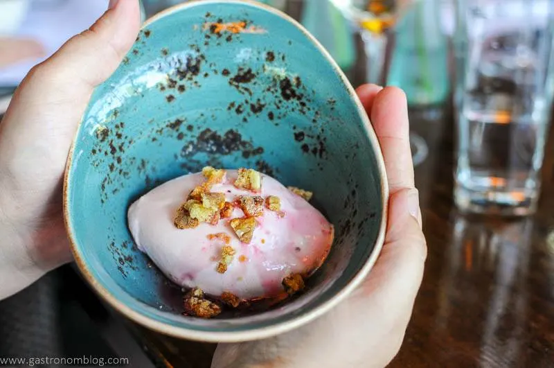 Pink ice cream topped with nuts in blue pottery bowl held by hands at Dante Restaurant Omaha