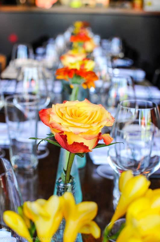 Yellow roses in vases with wine glasses and plates set along long table at Dante Restaurant Omaha