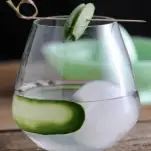Clear cocktail with ice ball in glass, cucumber slice