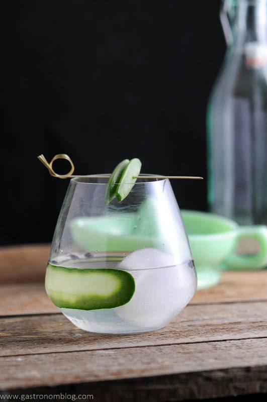Snap Pin Gin and Tonic Cocktail in glass with cucumber slices, pea on cocktail pick. Green juicer and bottle in background