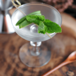 Clear cocktail in coupe with peas and mint. Wood spoon and tray
