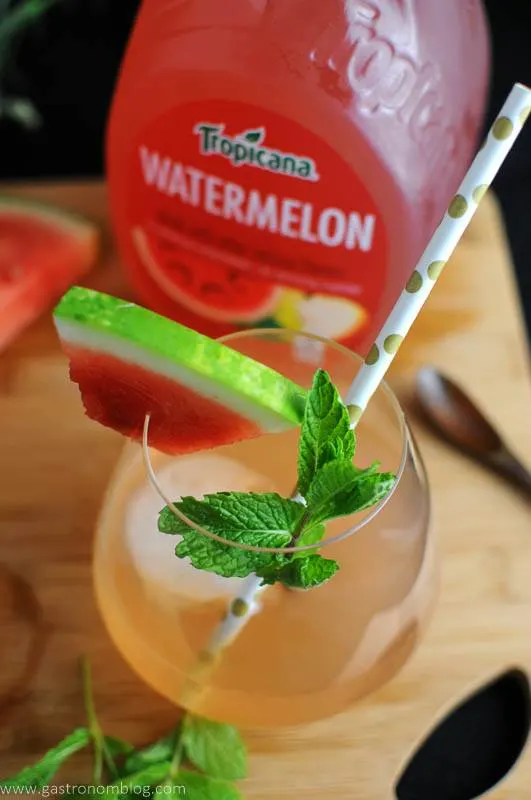 cocktail with gold dot straw, mint and watermelon wedge. Tropicana Watermelon Juice Bottle in background