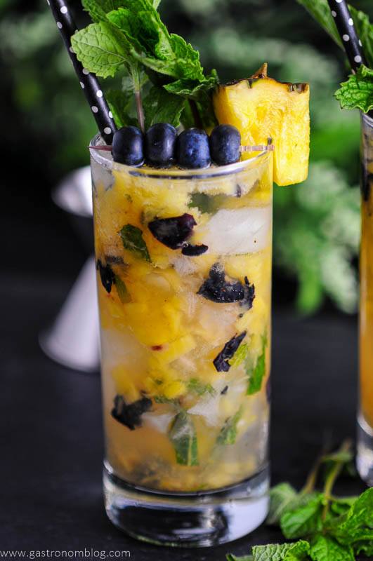 Blueberry Pineapple Mojito in highball glass with blueberries, pineapple wedge and mint. Black and white polka dot straw
