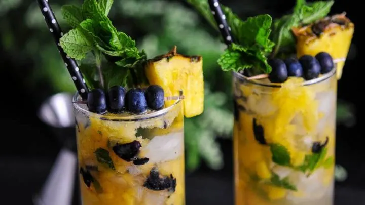 Blueberry Pineapple Mojito in 2 glasses with yellow pineapple and bluebrries. Mint on top