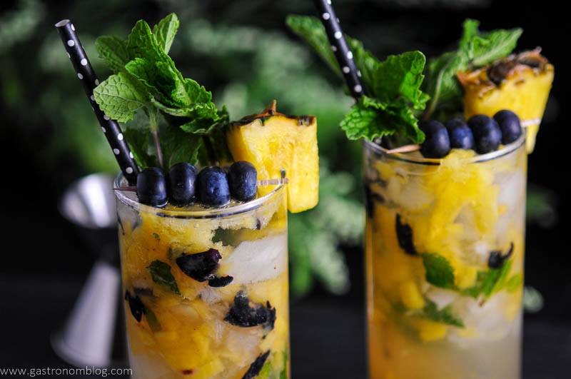 Blueberry Pineapple Mojitos in highballs glasses with pineapple wedges, blueberries, mint and white and black polka dot straws
