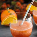 Orange cocktail in glass with orange slice and blue straw