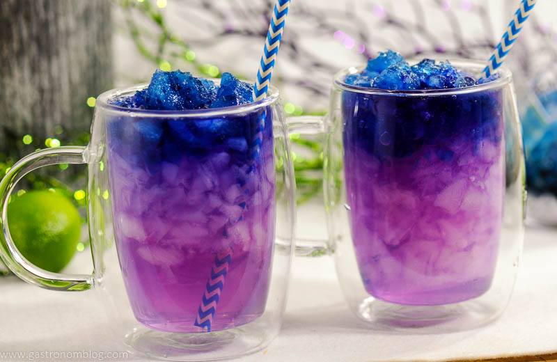 Galaxy Magic Moscow Mule Cocktail changes from blue to purple in clear glass mugs with blue straws. Limes in background. Color changing cocktail