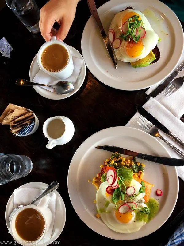 Top shot of white plates and cups of breakfast foods - eggs benedict, avocado toast and coffees