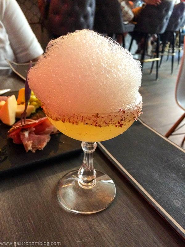Yellow cocktail in coupe with salt rim and pink foam