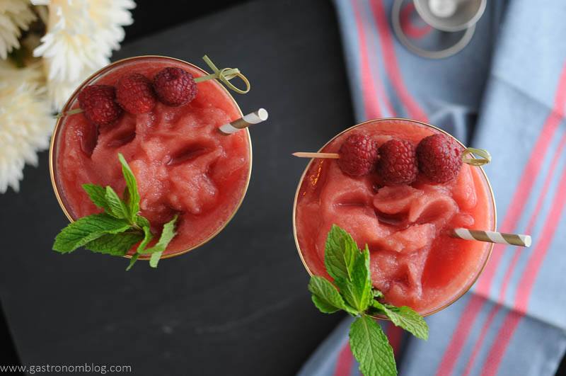 Watermelon Raspberry Frosé in coupes. Top shot with raspberries, mint and straws. On blue napkin with jigger