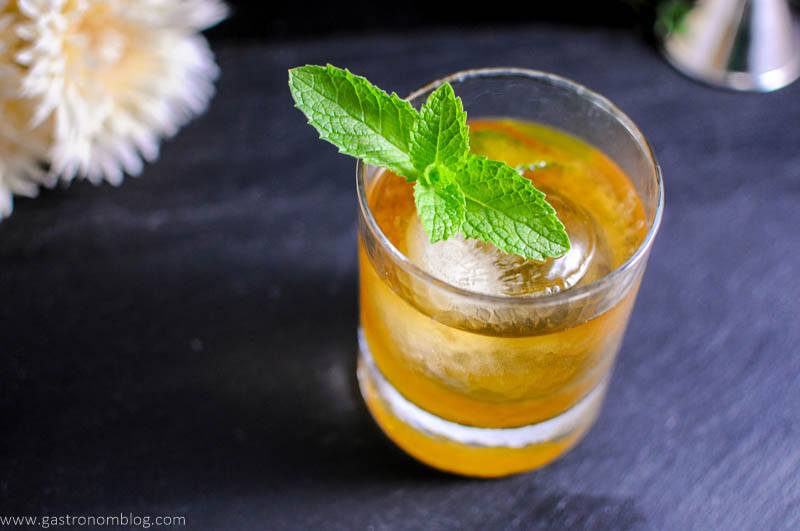 Apricot Honey Bourbon Sour Cocktail in rocks glass with mint leaves. Flowers in background