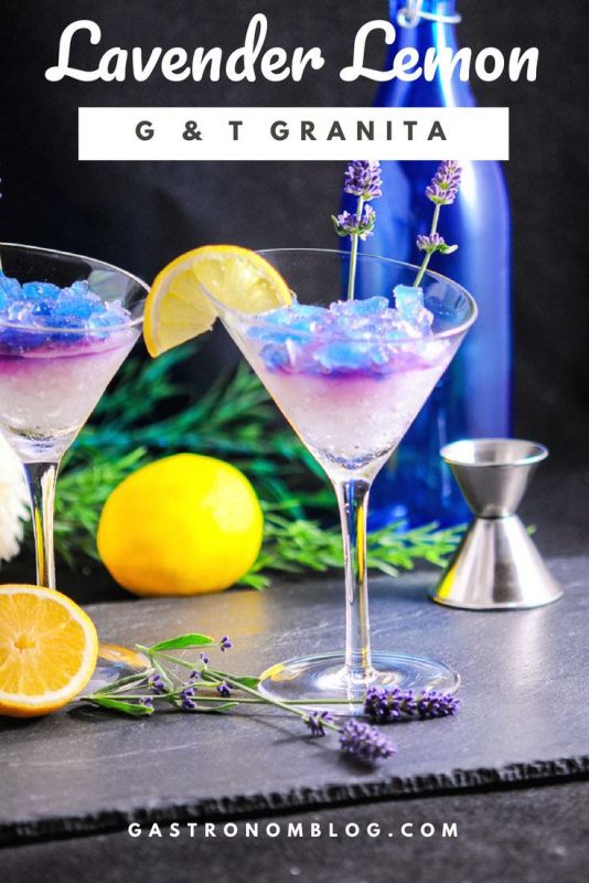 Lavender Lemon Gin and Tonic Granita Cocktail in martini glasses with blue ice. Lemon slice and lavender garnish. Jigger, lemon, greenery and blue bottle in background