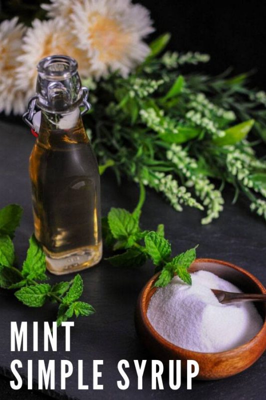 Bottle of mint simple syrup with bowl of sugar and greens behind
