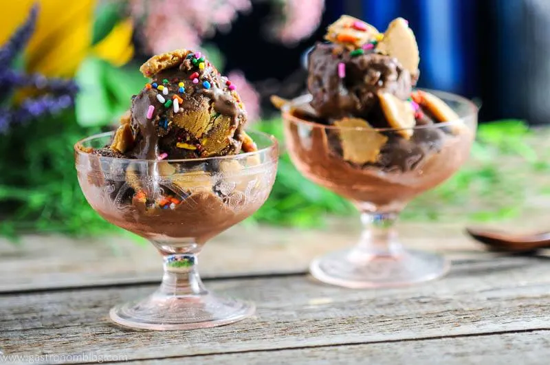 Dark Chocolate Vegan Ice Cream with Rum and No Bake Gluten Free Rainbow Sprinkle Cookie Crumble in pink glass dishes, wooden spoons and flowers in background