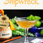 The Shipwreck Rum and Lillet Cocktail, gold cocktail with mint, rum bottle, wooden spoon, greenery in background