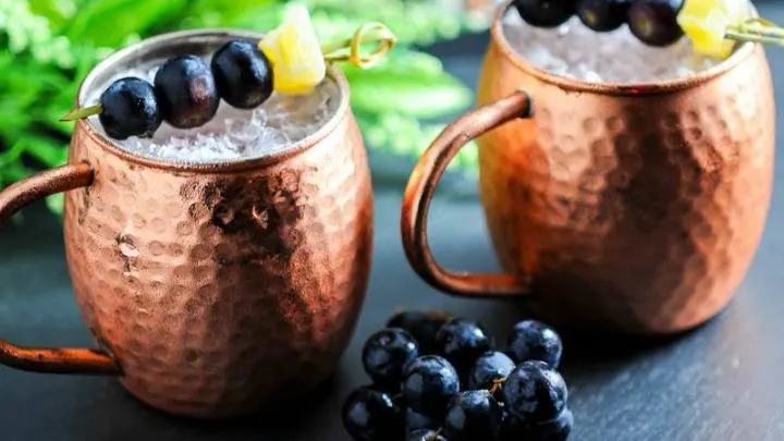Concord Grape Moscow Mule in copper mugs with grapes. Greenery in background