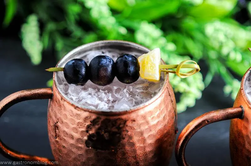 Concord Grape Moscow Mule in copper mug. Grapes and ginger on cocktail pick. Flowers in background