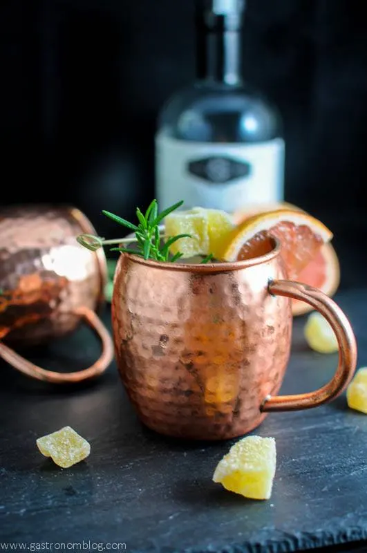 Rosemary Grapefruit Moscow Mule in copper mugs, grapefruit slices and candied ginger. Vodka bottle in background