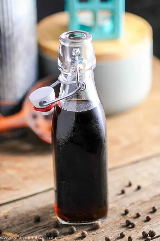 Homemade Allspice Dram in bottle with allspice berries on wood. Wood spoon in background