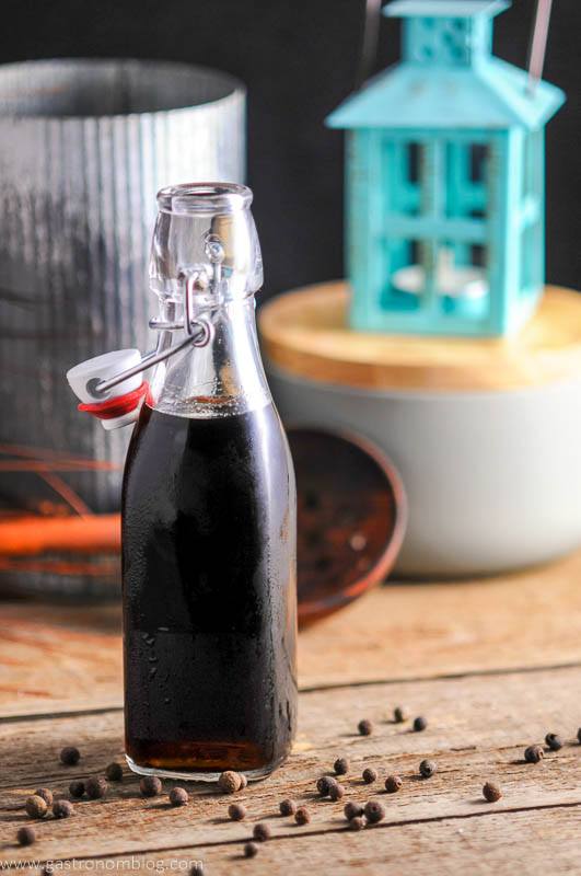 Homemade Allspice Dram, brown bottle, gray container, metal container and teal lantern behind