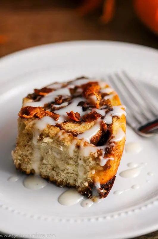 A fork sits next to bourbon bacon cinnamon rolls on a plate.