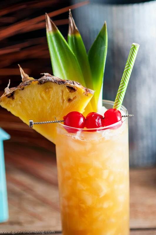 Close up shot of the Fall in Paradise Cocktail, garnished with candied cherries, pineapple and pineapple leaves, a tropical straw and crushed ice