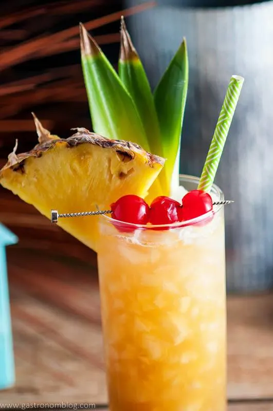 Close up shot of the Fall in Paradise Cocktail, garnished with candied cherries, pineapple and pineapple leaves, a tropical straw and crushed ice