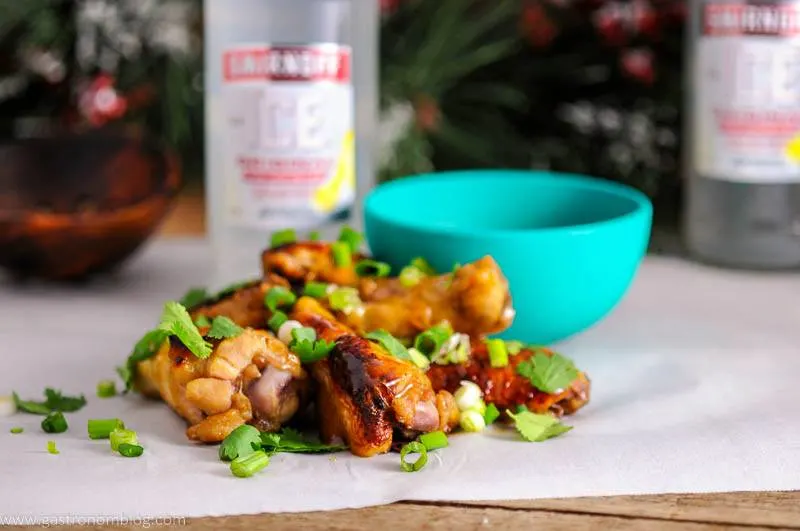 Citrus Asian Chicken Wings with green onion and cilantro on parchment paper. Green bowl with dipping sauce and Smirnoff bottle in background