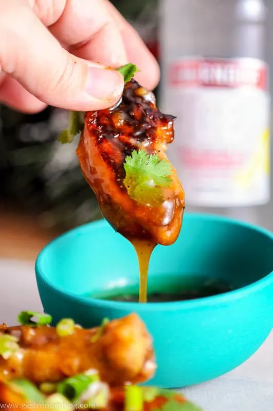 A citris Asian Chicken wing in a dipping sauce being held by a hand.