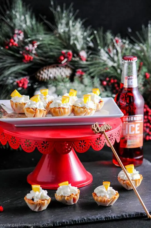 Mini Berry Bites on red cake stand and slate. With fir branch and strawberry Smirnoff Ice bottle in background.