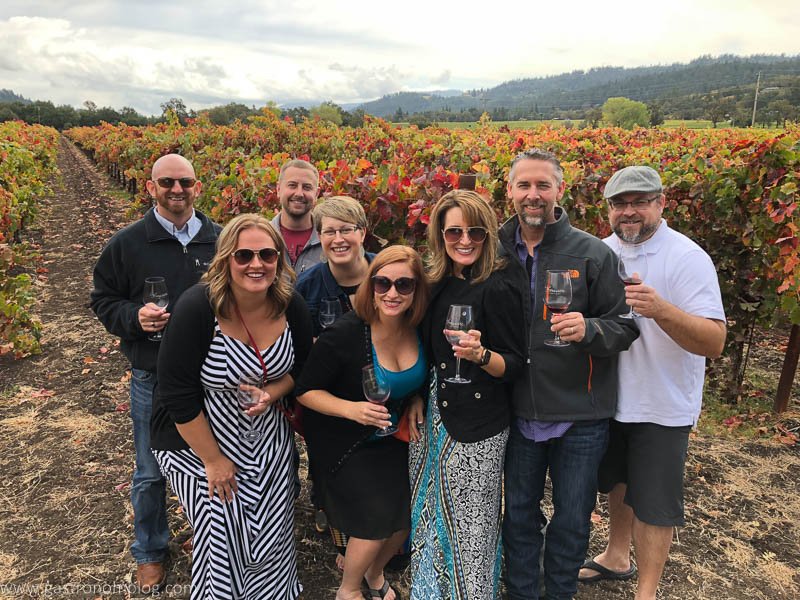 8 people standing in front of a fall vineyard holding wine glasses at one of the great Napa Valley Wineries
