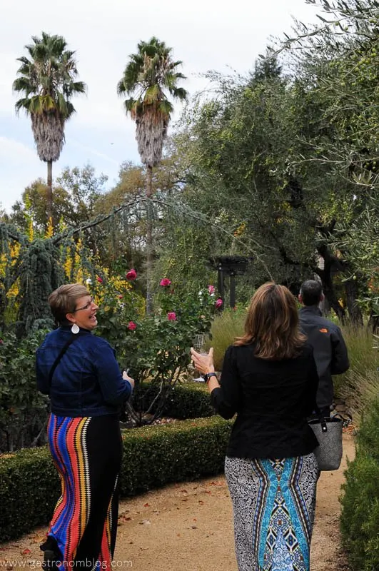 Ladies walking with wine glasses in Benessere Vineyards gardens with palm trees in the back