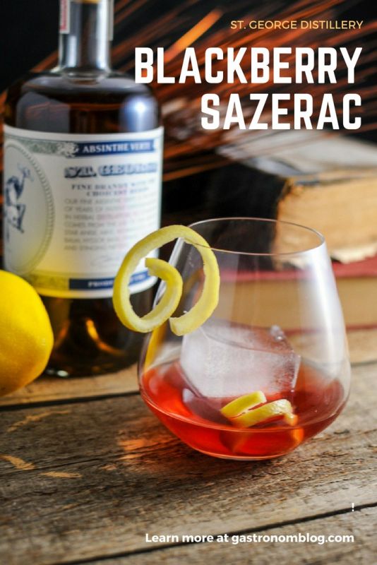 Blackberry Sazerac with St. George Distilling, red cocktail in glass with ice cube, lemon peels. Absinthe bottle behind