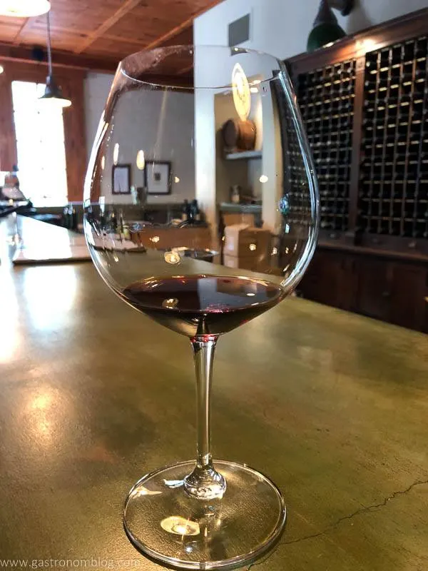 In the tasting room of Thomas George Estates, a glass of red wine on concrete counter