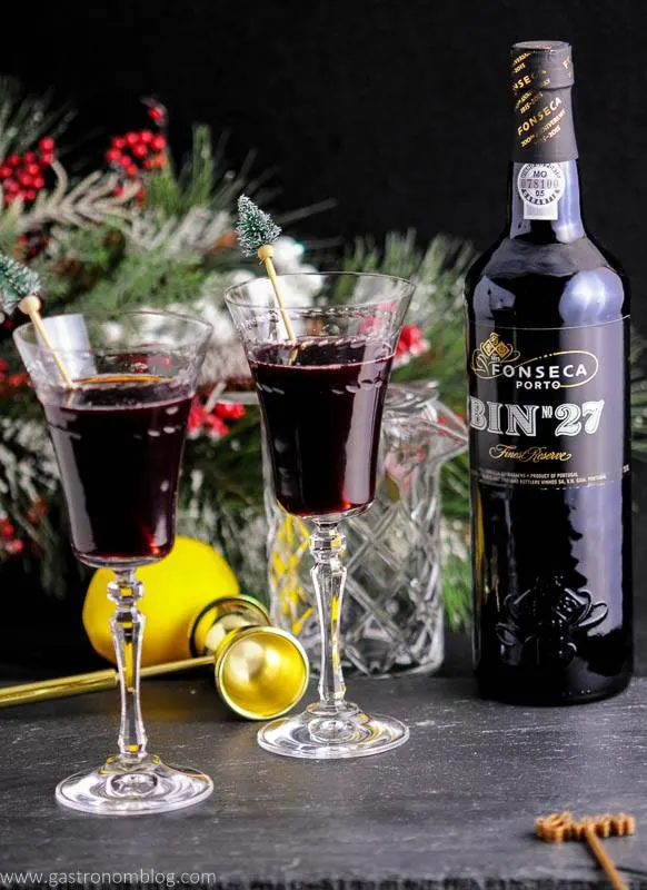 Two Recap Cocktails, made with Bin 27 Port Wine, amaro, mint and lemon sits in front of holiday decor, a gold double jigger and a bottle of port wine.