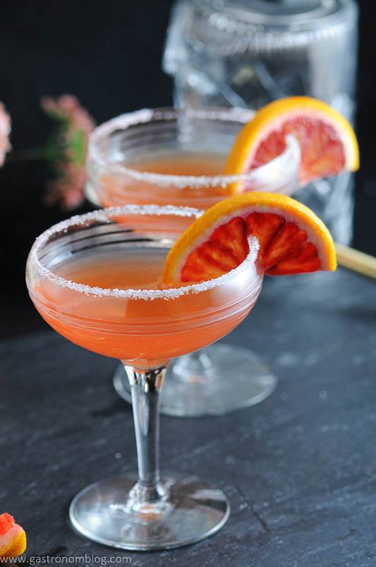 Blood orange sidecars in vintage cocktail coupe and garnished with blood orange wheels. Mixing glass in background