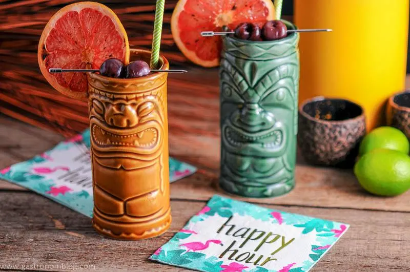 A pair of tiki glasses full of The Rambler's Ruby, a tiki cocktail made with Gin and Mezcal.