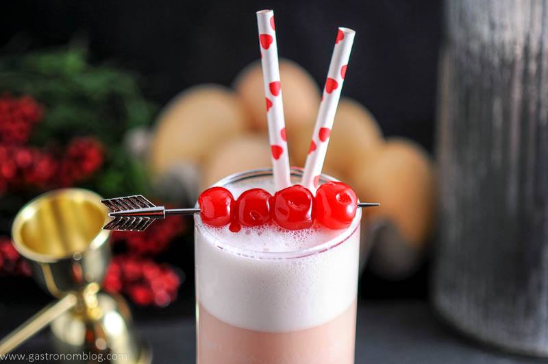 an arrow cocktail pick pieces maraschino cherries that garnish a Cherry Toasted Cream Ramo Gin Fizz with straws