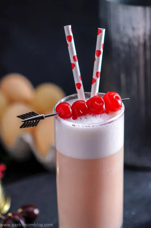 Cherry Toasted Cream Ramos Gin Fizz - gin, cherry liqueur, egg white, simple syrup, lemon juice, orange flower water, toasted cream, club soda, lime juice, cherry juice. A classic cocktail from New Orleans, our Ramos Gin Fizz uses the Instant Pot for the toasted cream from Gastronomblog. #cocktail #cocktails #drink #drinks #NewOrleans #instantpot #gin #recipes #clubsoda #gastronomblog an arrow cocktail pick pieces maraschino cherries that garnish a Cherry Toasted Cream Ramos Gin Fizz