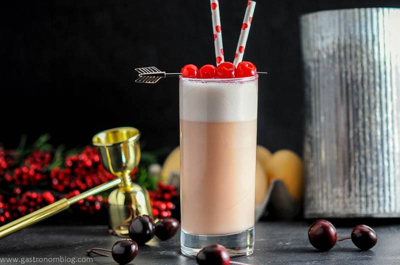 A highball glass with a Cherry Toasted Cream Ramos Gin Fizz , double jigger and fresh cherries