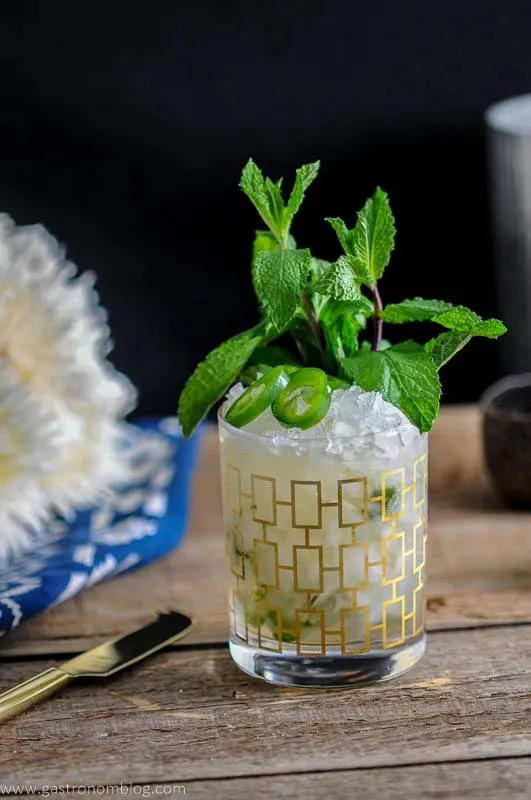 This Mezcal Mint Julep is in a gold rocks glass with crushed ice, jalapeno slices and a mint bunch.