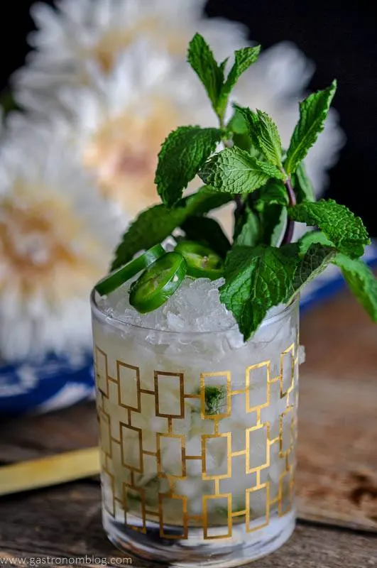 This Mezcal Mint Julep is in a gold rocks glass with crushed ice, jalapeno slices and a mint bunch.