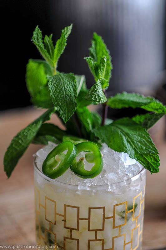 This Mezcal Mint Julep is in a gold rocks glass with crushed ice, jalapeno slices and a mint bunch.