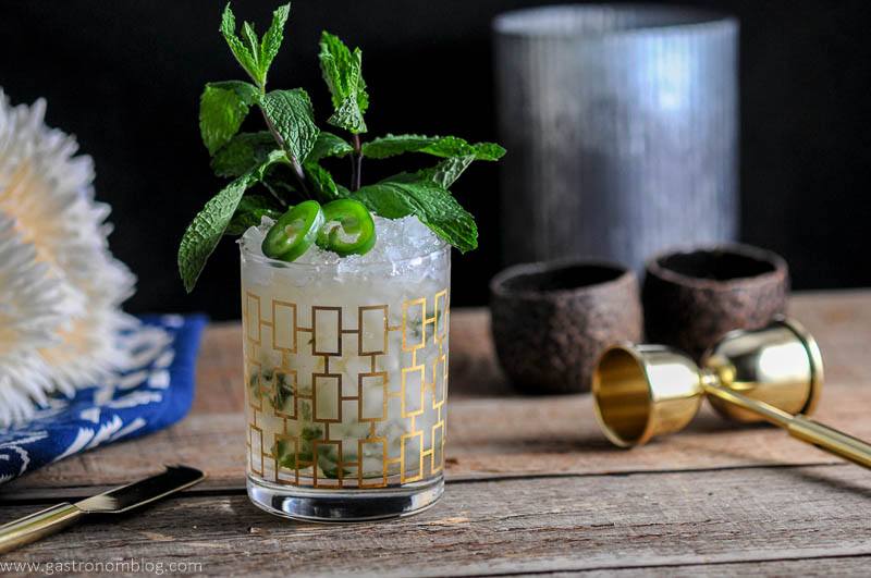 This Mezcal Mint Julep is in a gold rocks glass with crushed ice, jalapeno slices and a mint bunch.