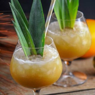 Coconut Rum Painkillers, orange cocktails in glasses with ice and pineapple fronts, yellow straws