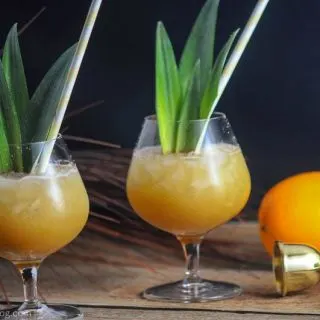 Coconut Rum Painkillers in glasses with crushed ice, pineapple fronds and yellow straws