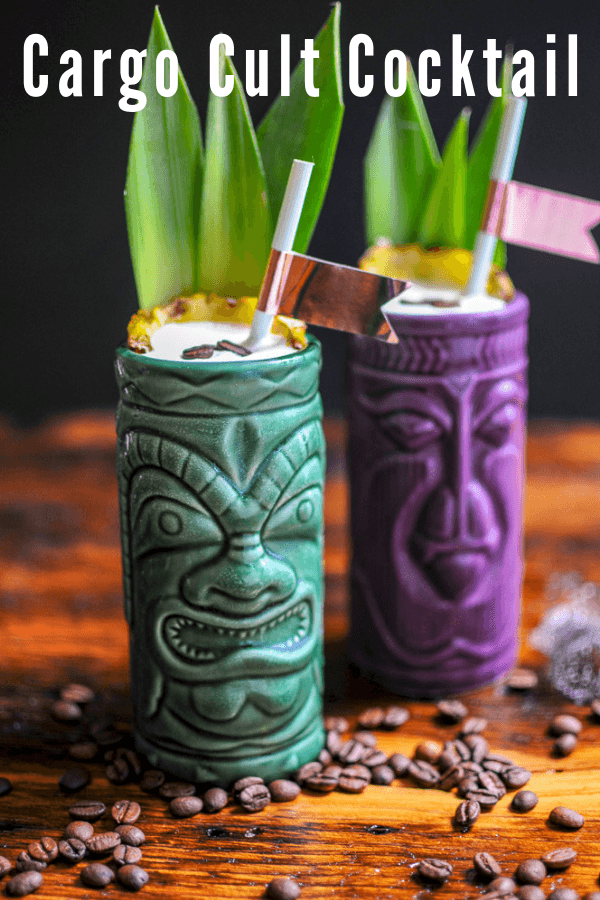 Green and purple tiki mugs with coconut cream and coffee beans on top, pineapple fronds and straws. Coffee beans on wooden table