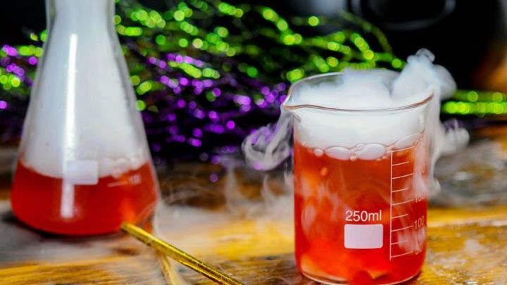 Dry ice cocktail, smoke coming out of beaker of red cocktail on wood table