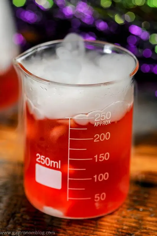 Dry ice cocktail, smoke coming out of beaker of red cocktail on wood table